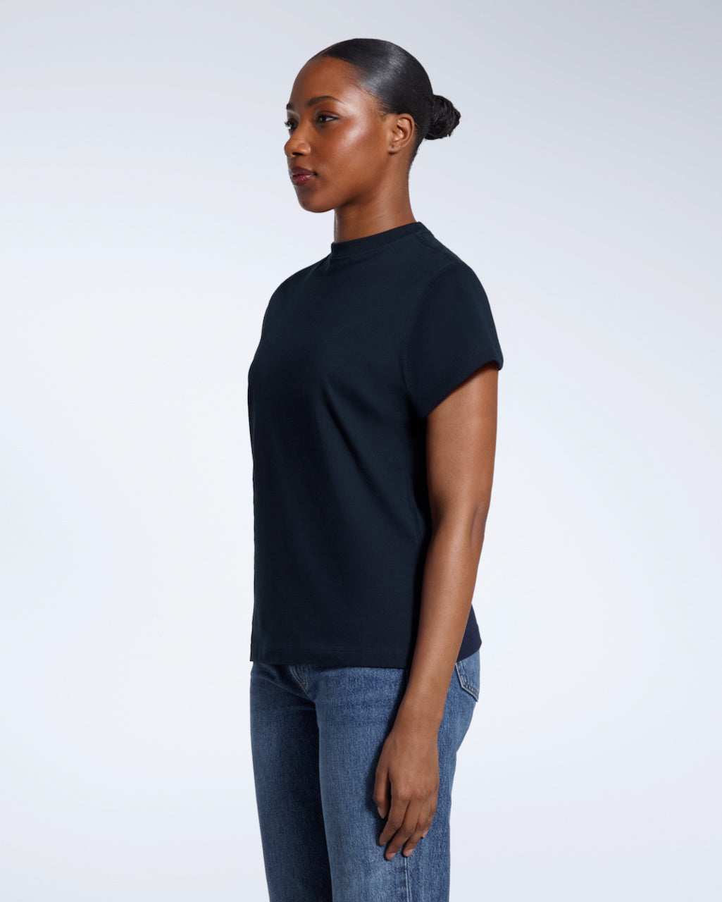 A woman looking away from the camera with her arms by her sides, modelling a plain navy short sleeve organic cotton t shirt.