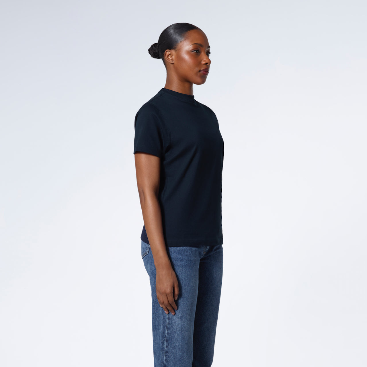 A woman looking away from the camera with her arms by her sides, modelling a plain navy short sleeve organic cotton t shirt.