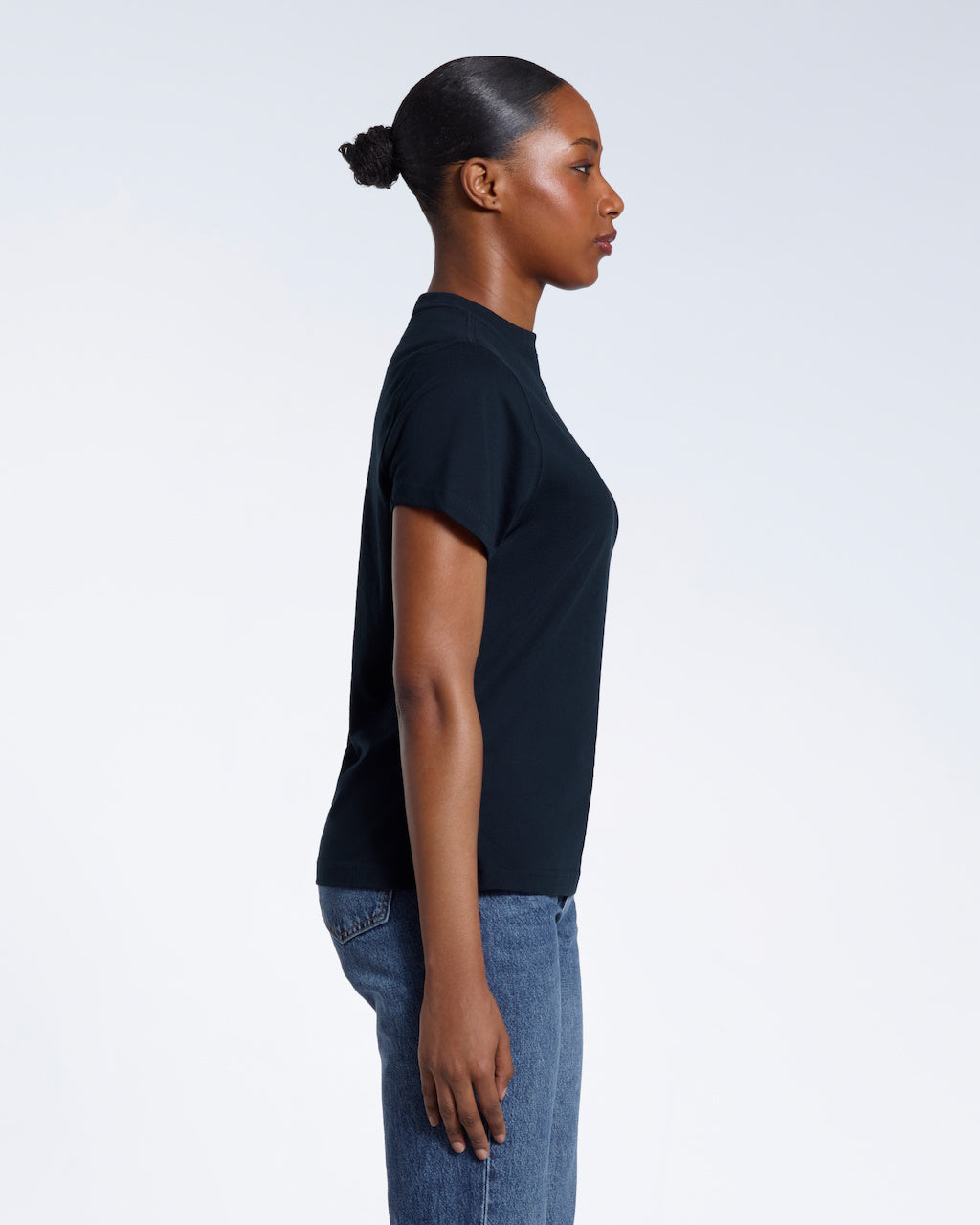 A woman facing side on with her arms by her sides, modelling a plain navy short sleeve organic cotton t shirt.