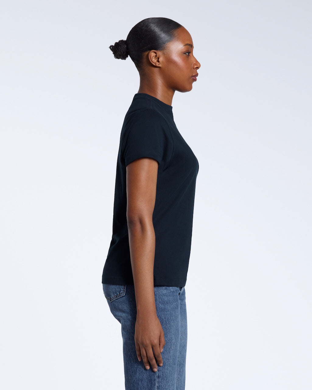 A woman facing side on with her arms by her sides, modelling a plain navy short sleeve organic cotton t shirt.