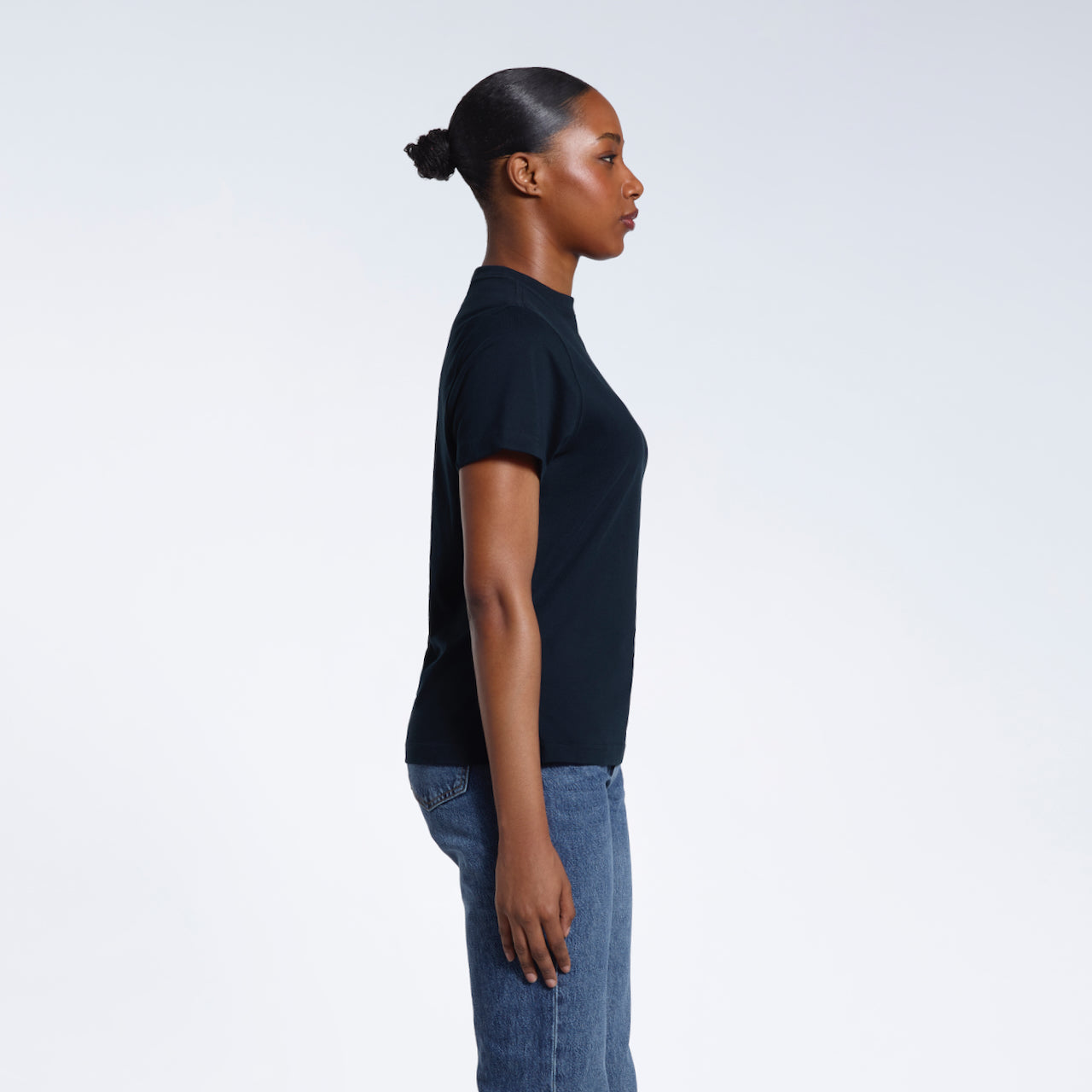 A woman facing side on with her arms by her sides, modelling a plain navy short sleeve organic cotton t shirt.