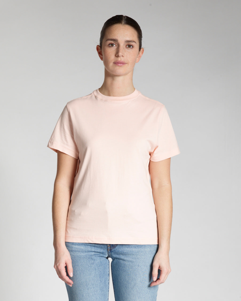 A woman facing front on, modelling a plain pink, short sleeve organic cotton t shirt.