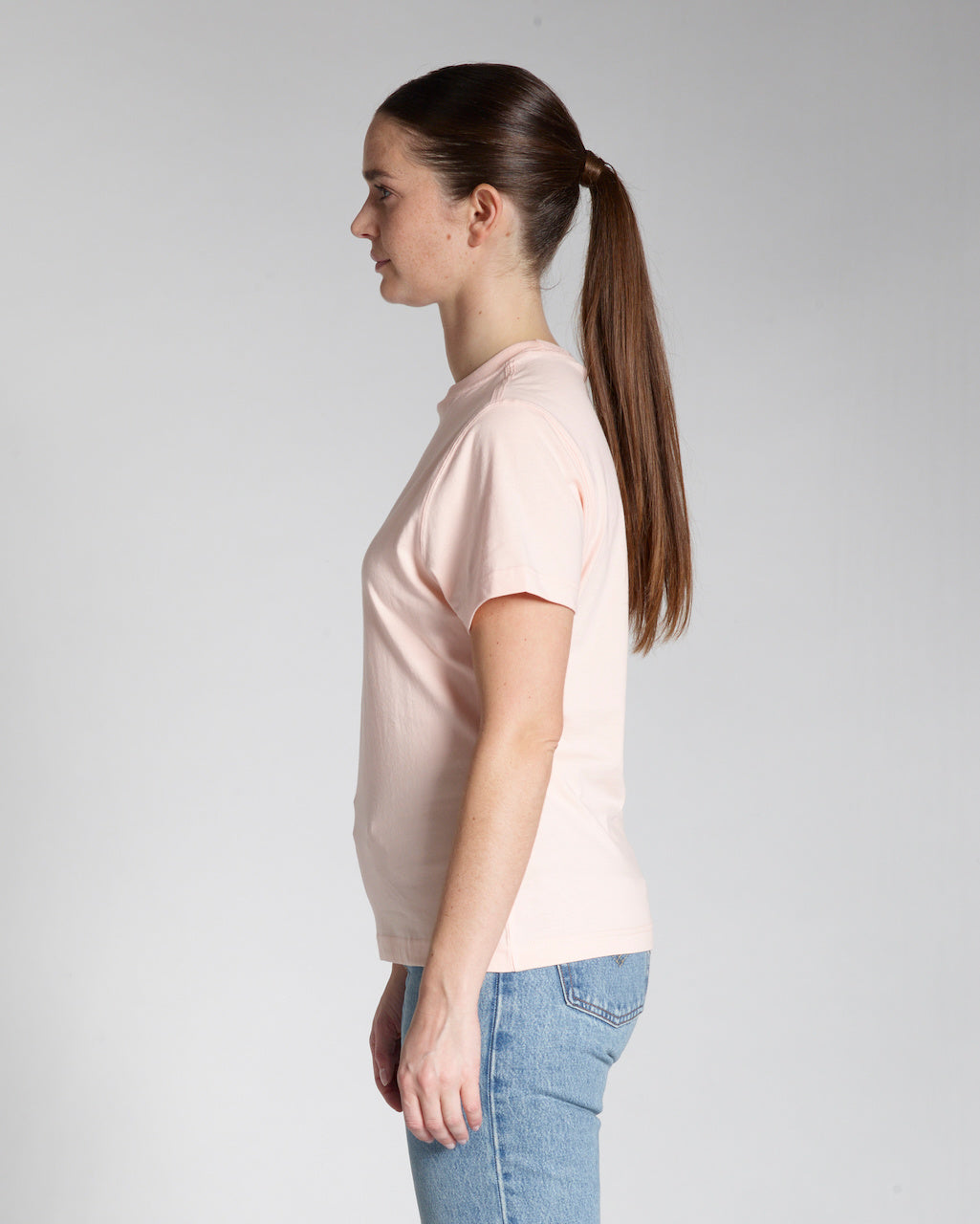 A woman facing side on, modelling a plain pink, short sleeve organic cotton t shirt.