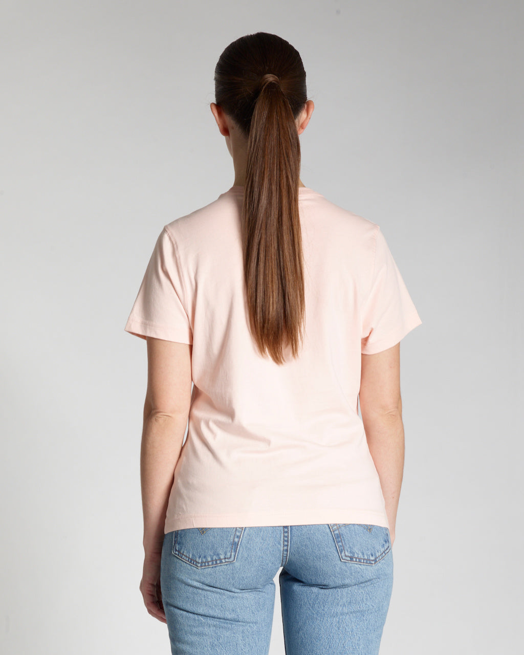 A woman facing away from the camera, modelling a plain pink, short sleeve organic cotton t shirt.