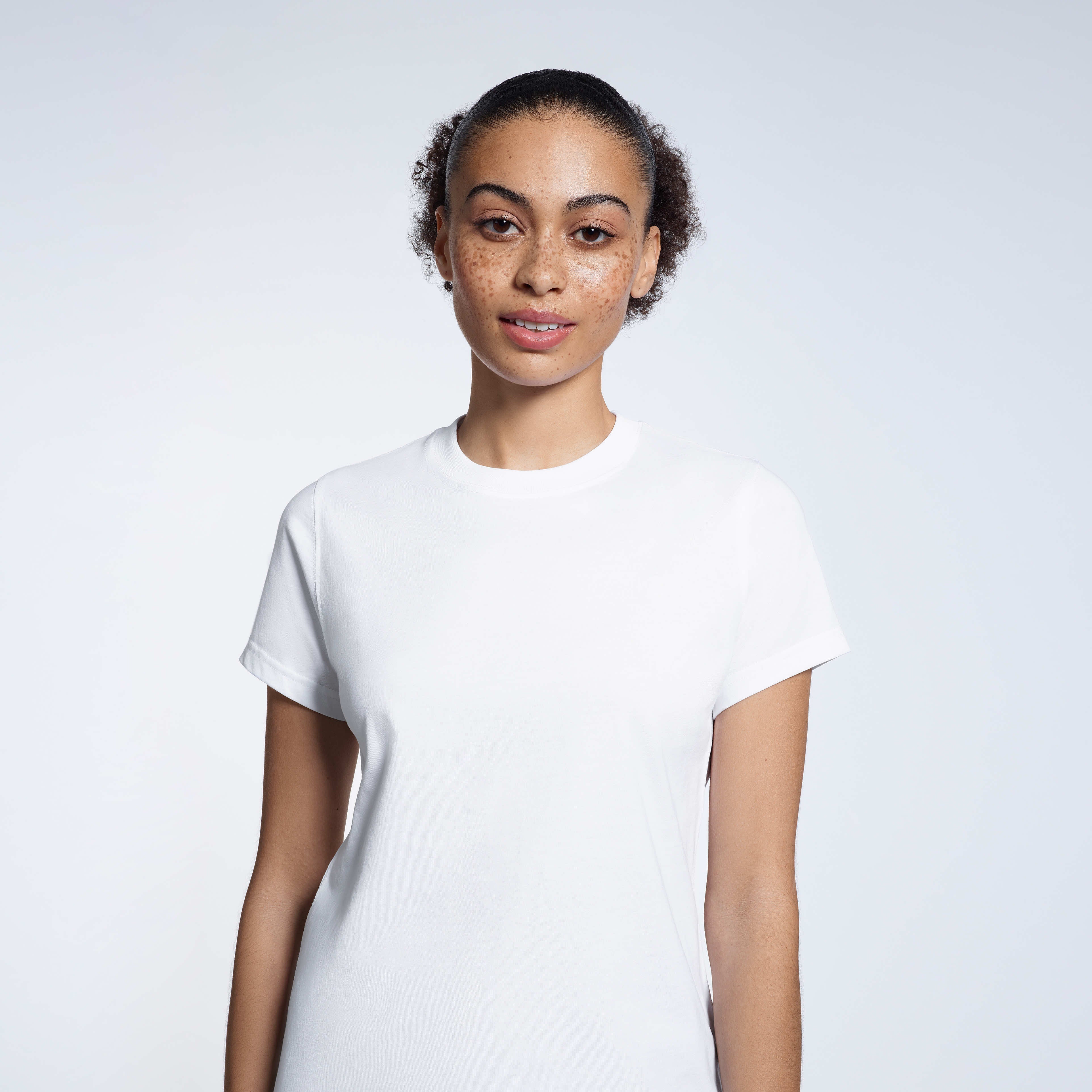 A woman looking into the camera, modelling a plain white short sleeve organic cotton t shirt.