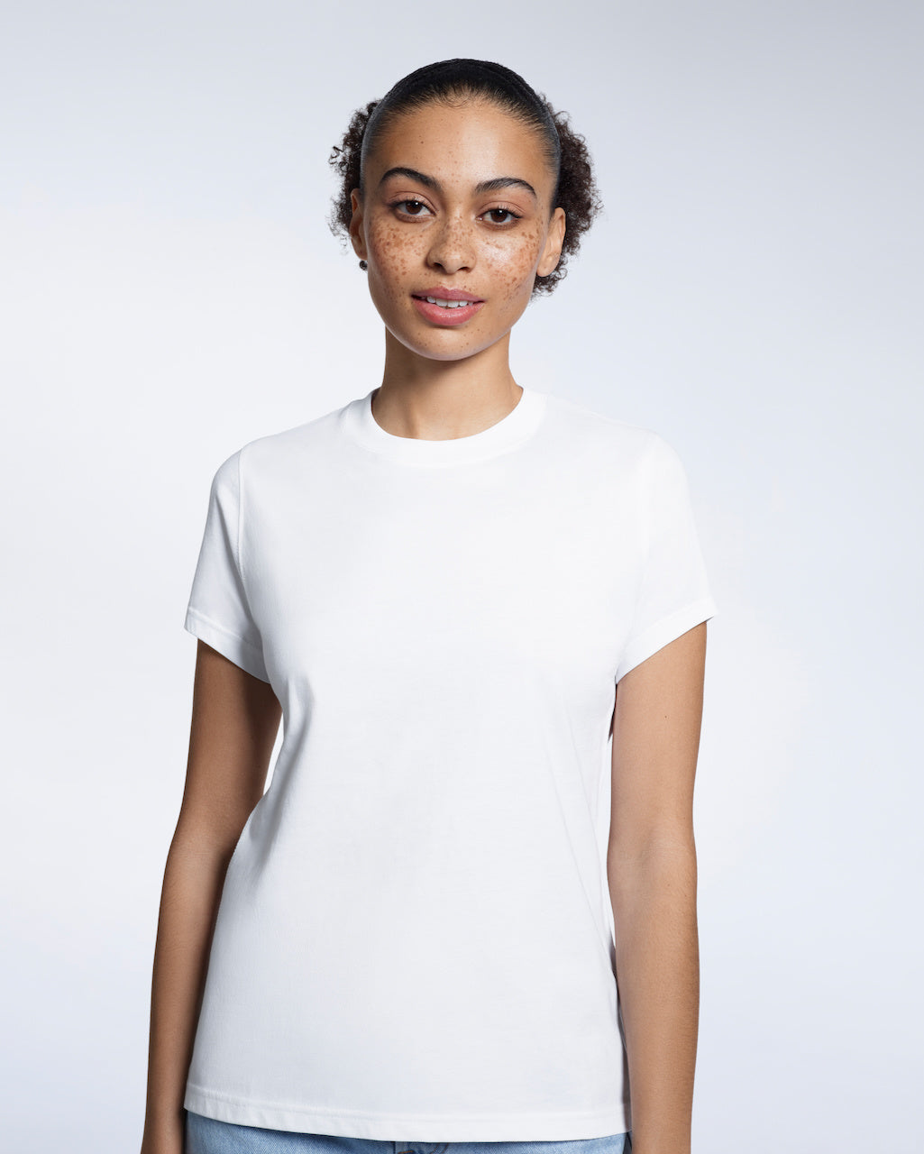 A woman looking into the camera, modelling a plain white short sleeve organic cotton t shirt.