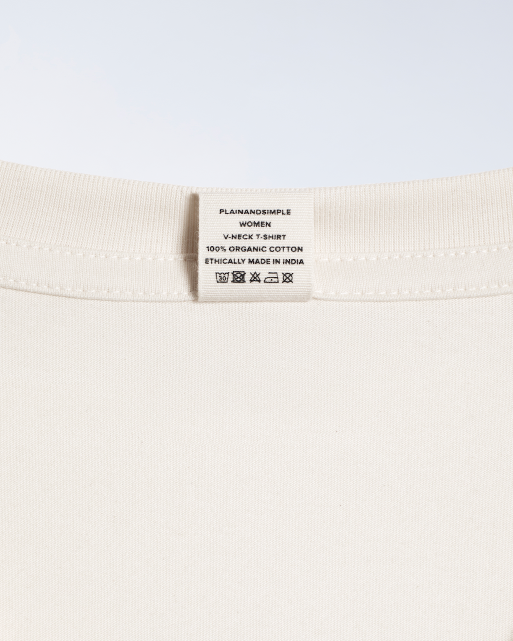A close up of the neck label of a natural coloured, v neck, organic cotton t shirt.