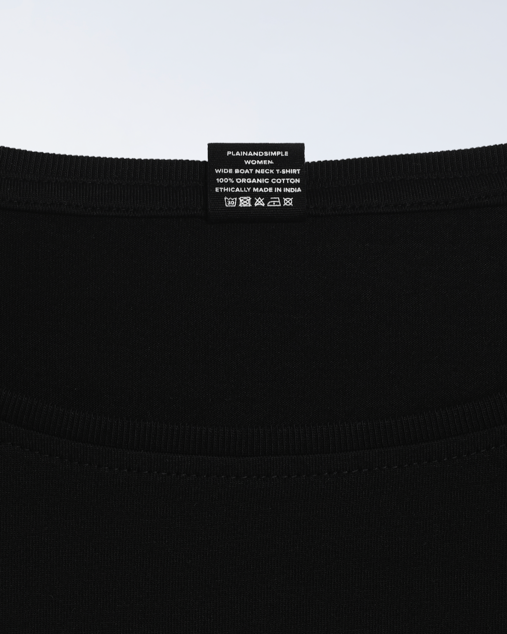 A close up of the neck label in a black, wide boat neck, organic cotton t shirt.