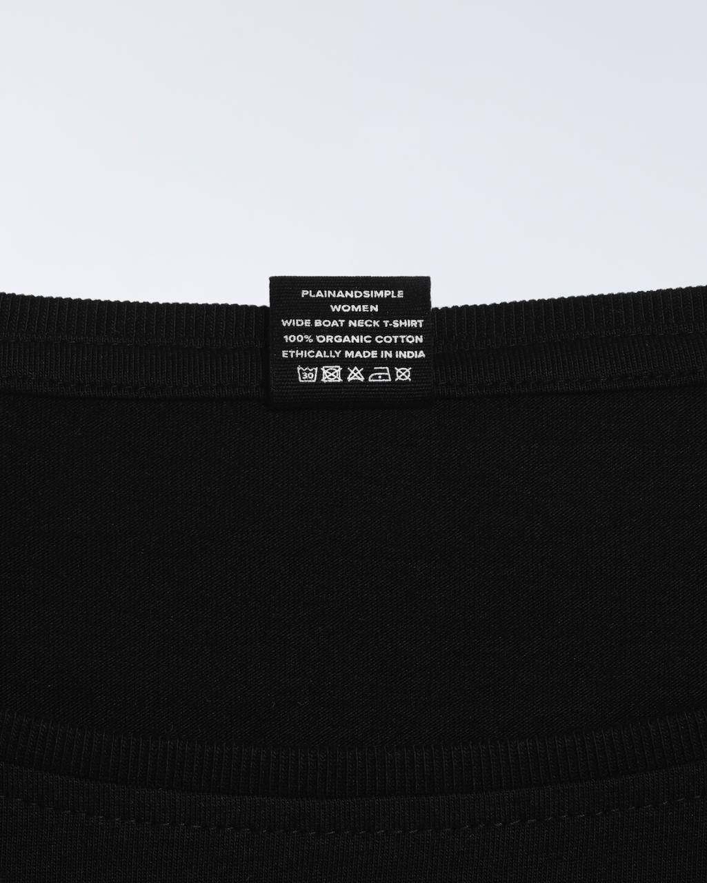 A close up of the neck label in a black, wide boat neck, organic cotton t shirt.