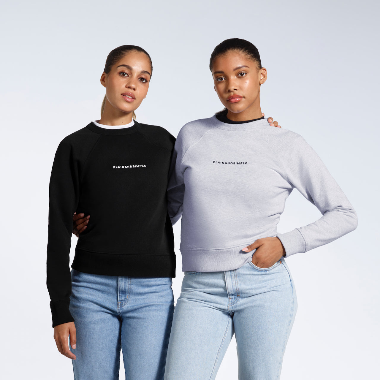 Two women looking at the camera with their arms round eachother, modelling branded black and grey, heavyweight organic cotton sweatshirts.