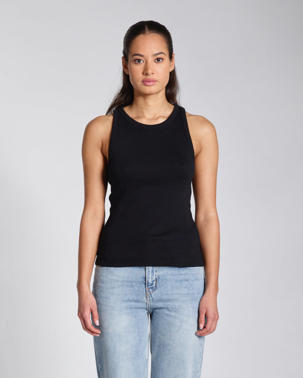 A woman facing front on, modelling a plain black, organic cotton tank top.