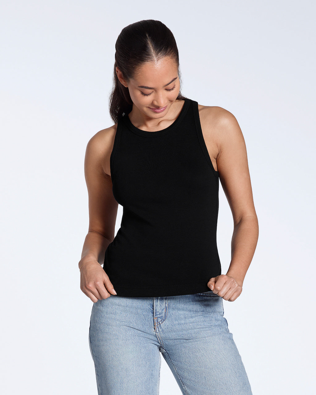 A woman looking down, modelling a plain black, organic cotton tank top.