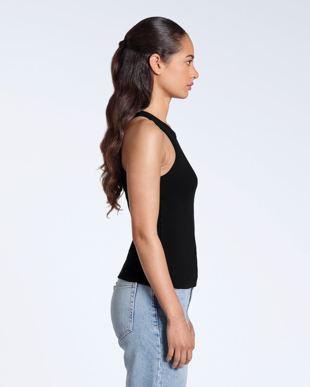 A woman facing side on, modelling a plain black, organic cotton tank top.