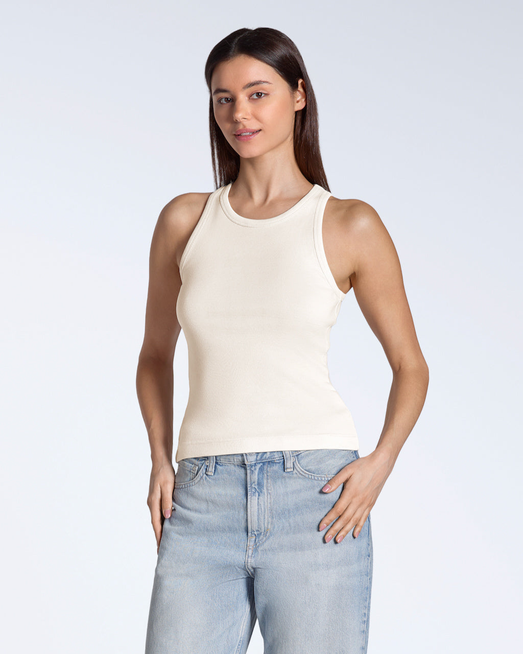 A woman smiling into the camera, modelling a plain natural coloured, organic cotton tank top.
