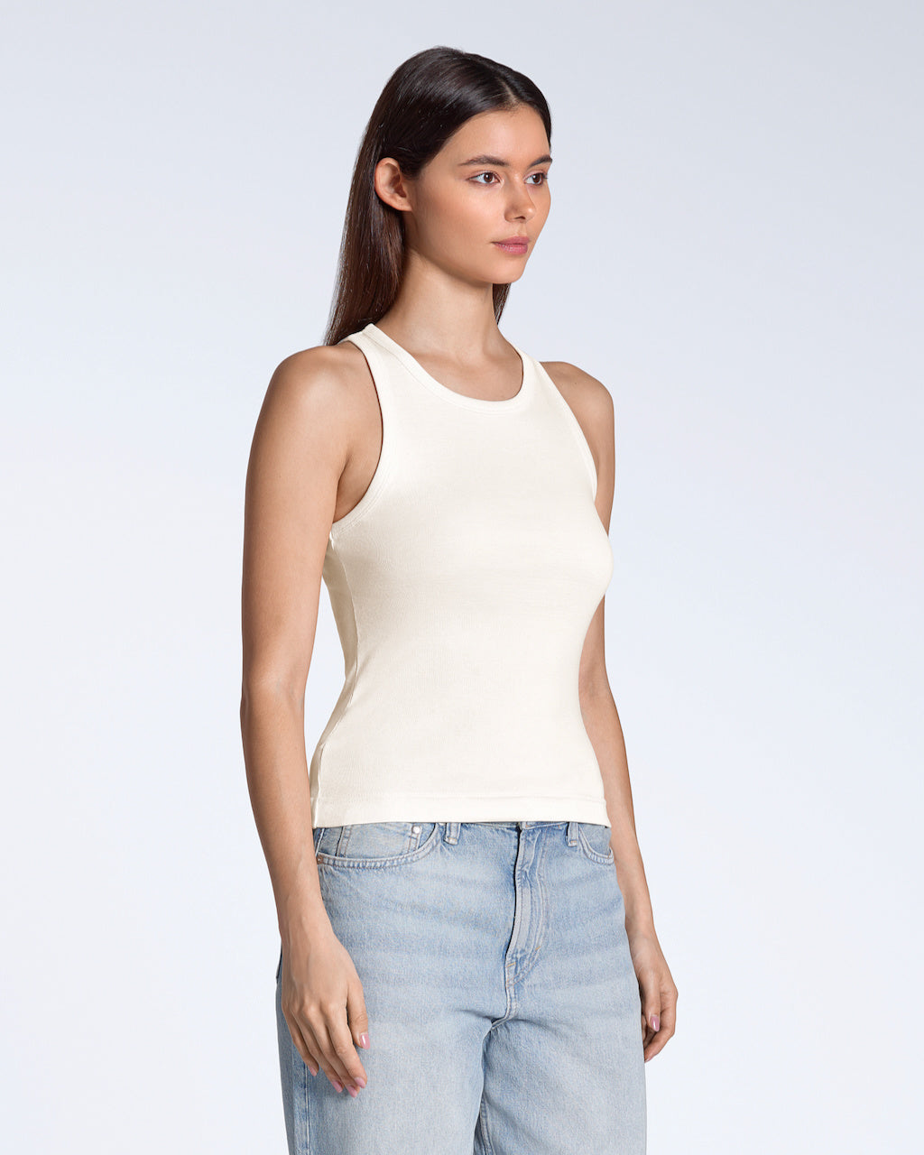 A woman at an angle with her arms by her sides, modelling a plain natural coloured, organic cotton tank top.