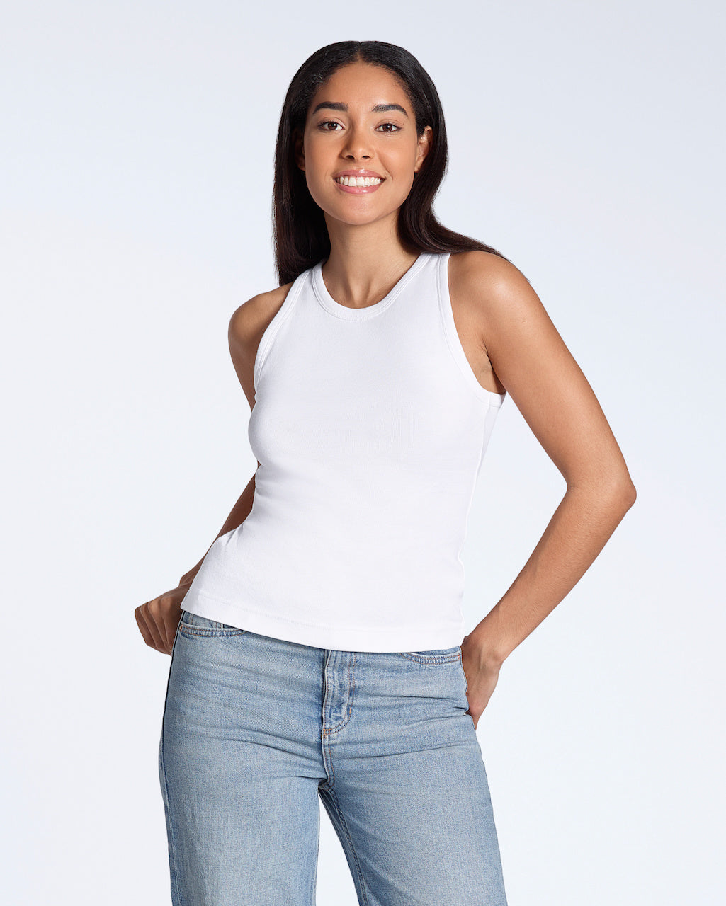 A woman smiling into the camera, modelling a plain white, organic cotton tank top.
