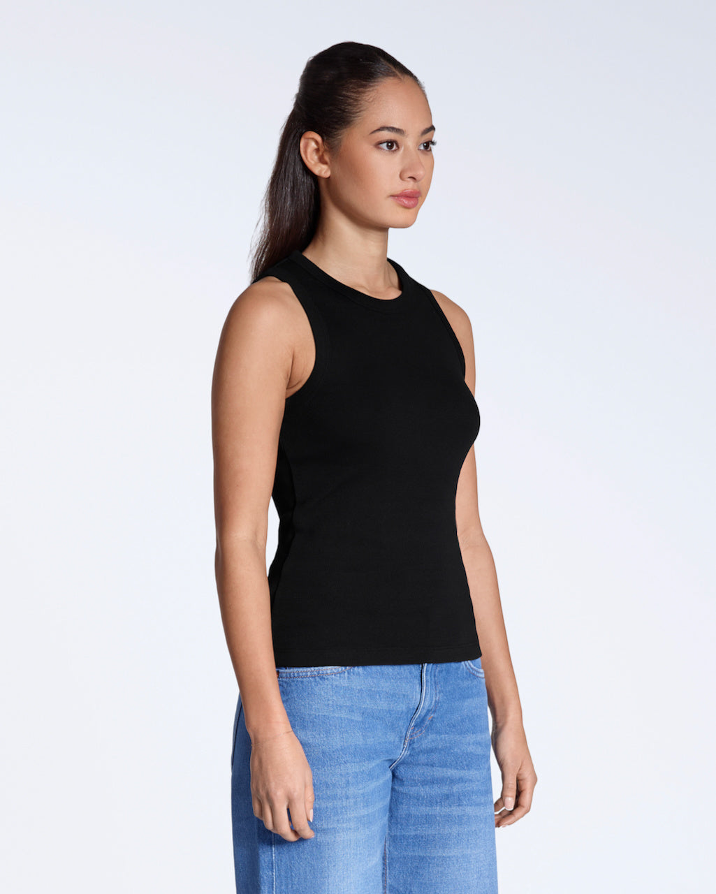 A woman at an angle with her arms by her sides, modelling a plain black organic cotton tank top.