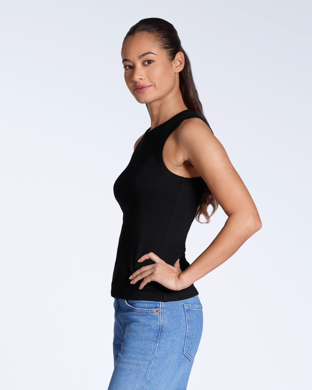 A woman facing side on, smiling into the camera, modelling a plain black, organic cotton tank top.