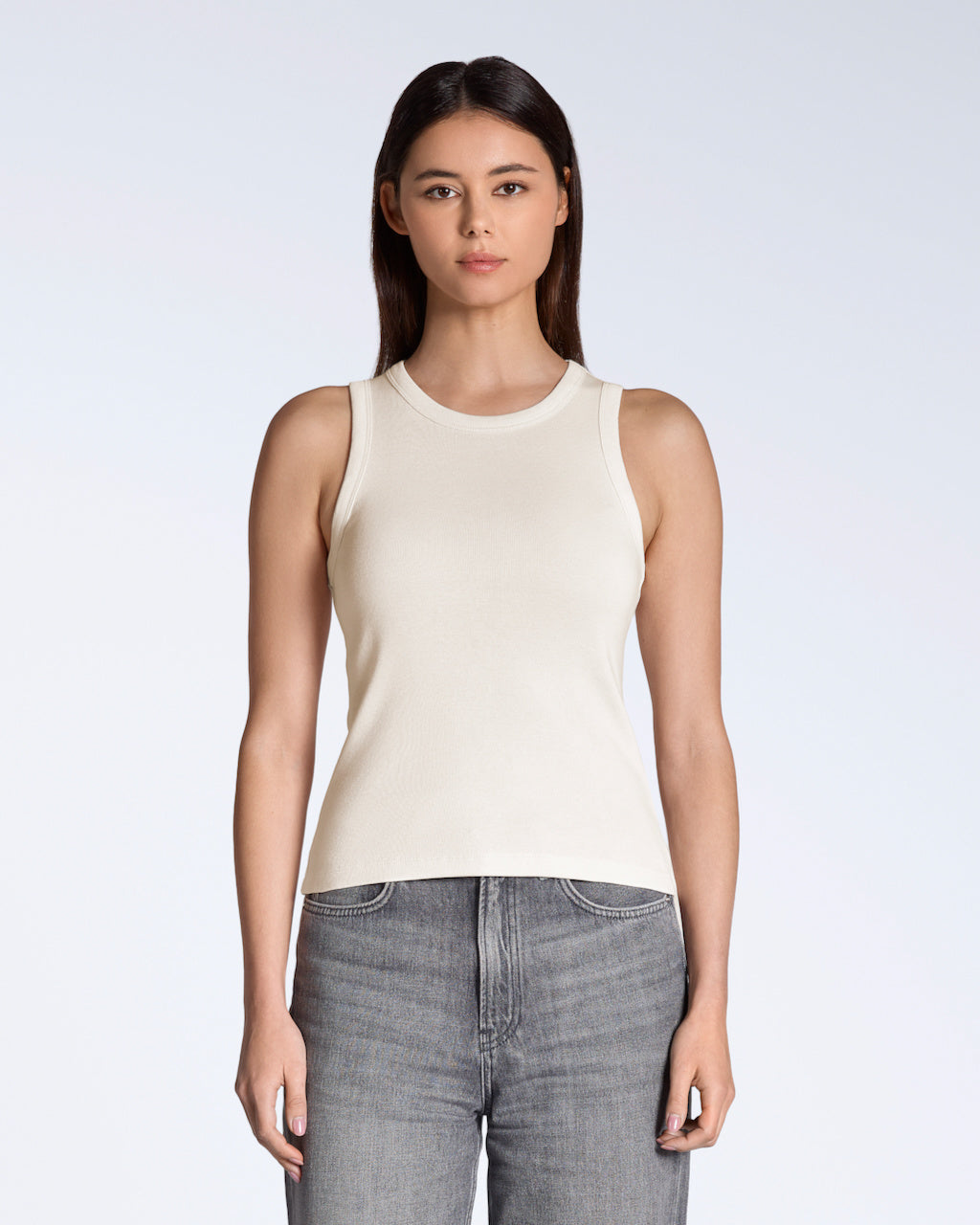 A woman facing front on, modelling a plain natural coloured, organic cotton tank top.