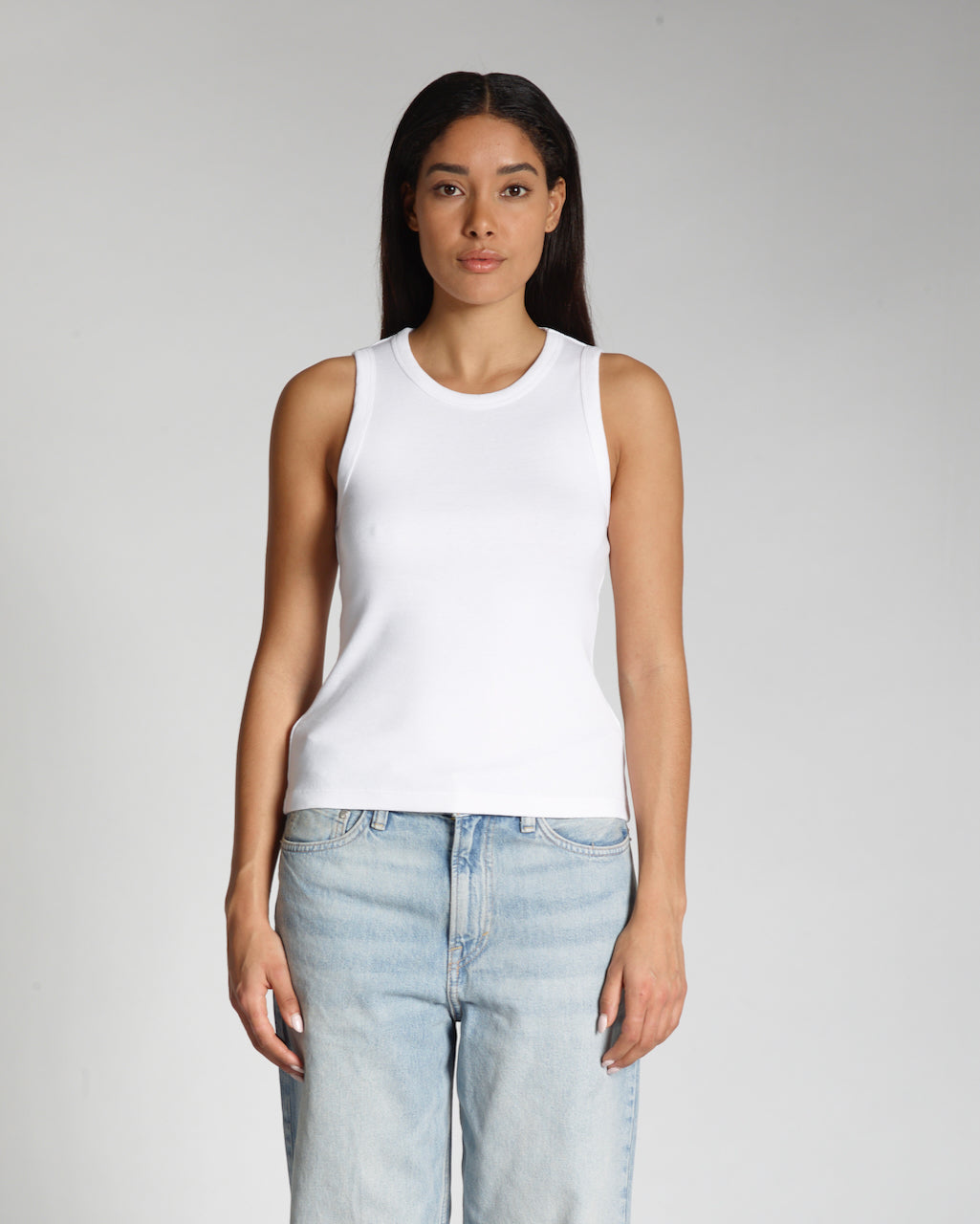A woman facing front on, modelling a plain white, organic cotton tank top.