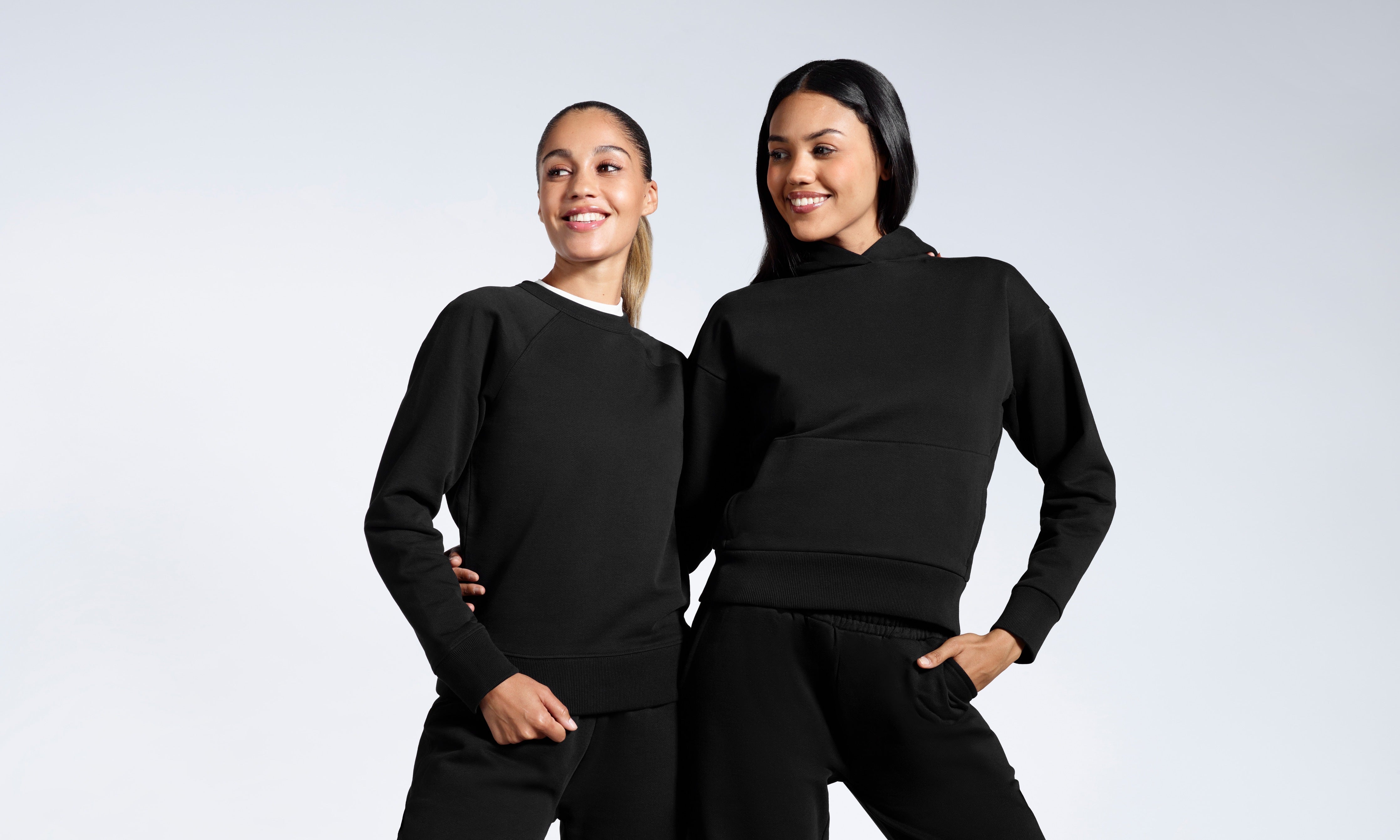 Two women in a plain black tracksuit set, smiling against a grey background.