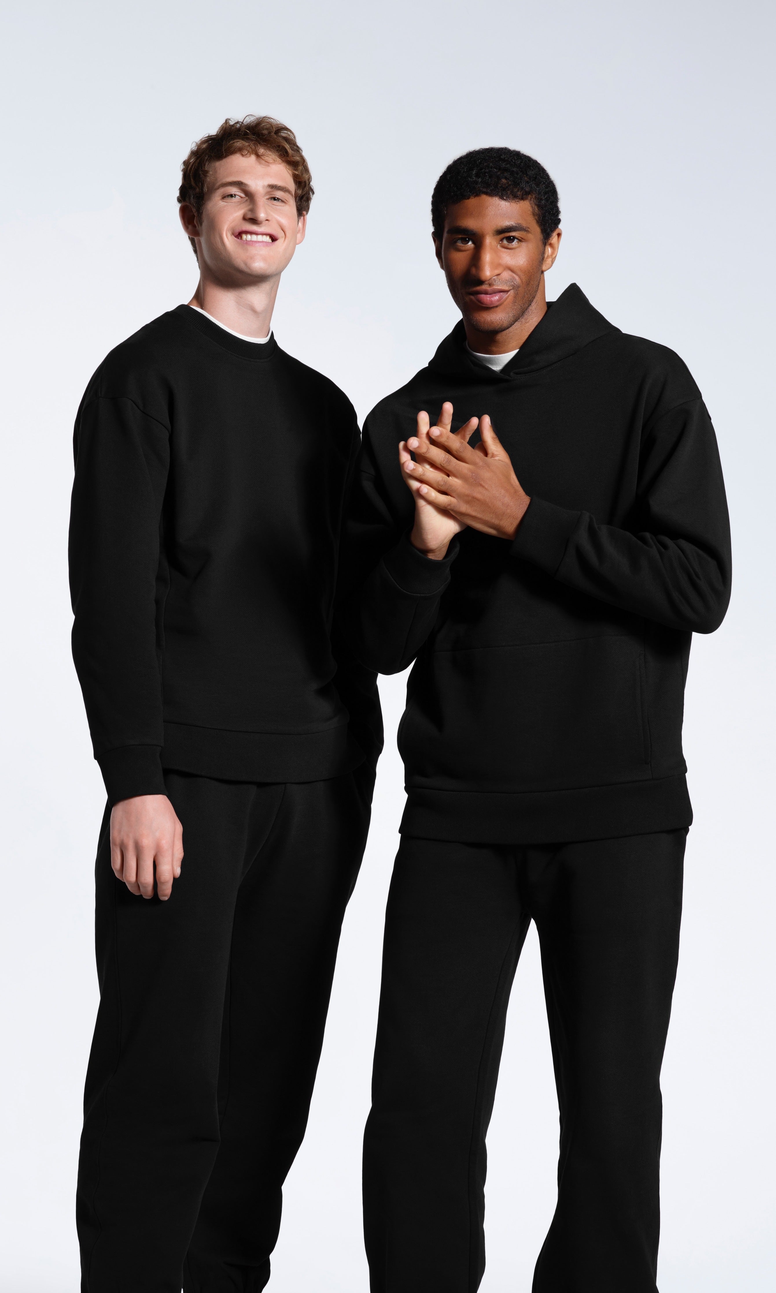 Two men modelling plain black heavyweight, organic cotton tracksuit sets.