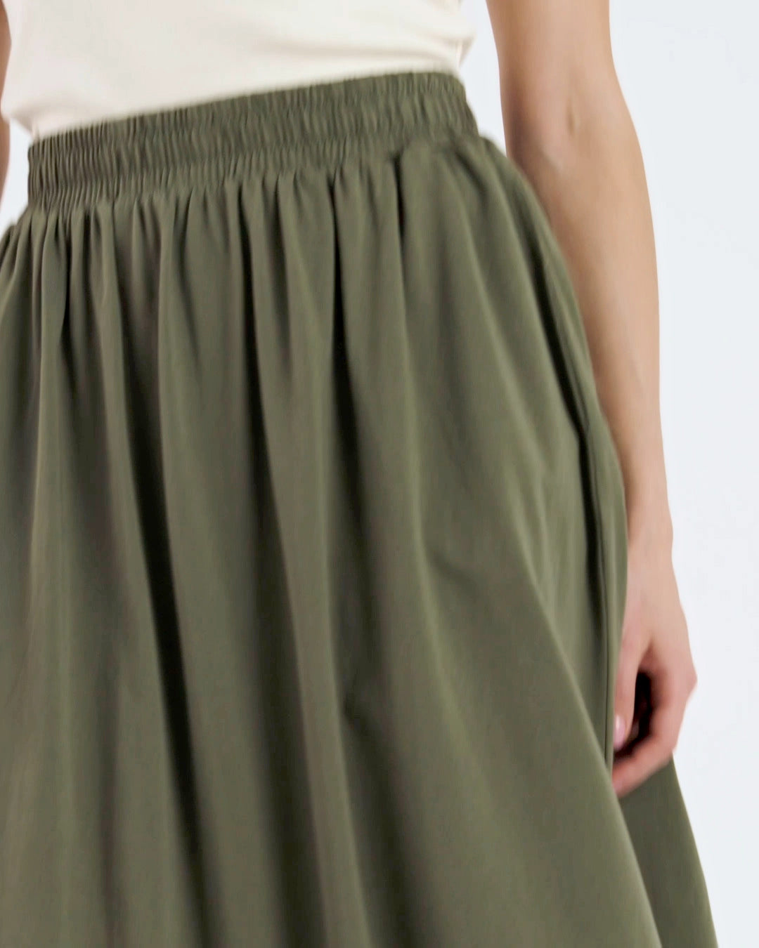 A compilation of short video clips of a woman modelling a plain olive green, organic cotton midi skirt.