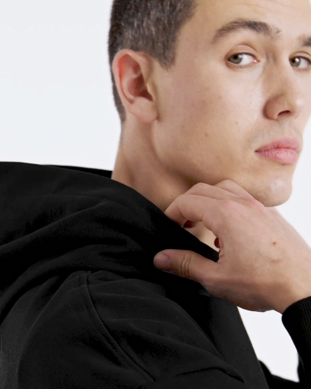 A compilation of short video clips of a man modelling a plain black, oversized organic cotton hoodie with a pair of blue jeans.